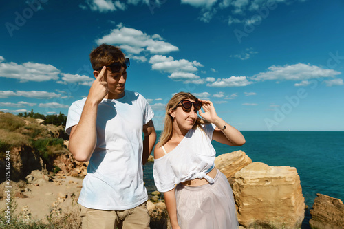lovely young adult couple in glasses on the rocks in the sea near the beach with big cliffs, Black Sea, Odessa, Ukraine, place for text set