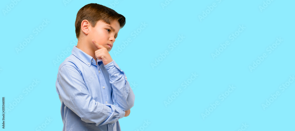 Handsome toddler child with green eyes doubt expression, confuse and wonder concept, uncertain future over blue background Handsome toddler child with green eyes doubt expression, confuse and wonder concept, uncertain future over blue background