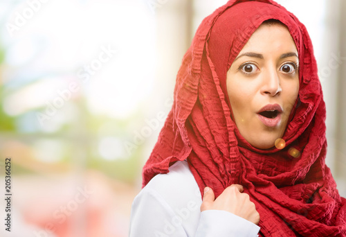 Young arab woman wearing hijab happy and surprised cheering expressing wow gesture, pointing with finger