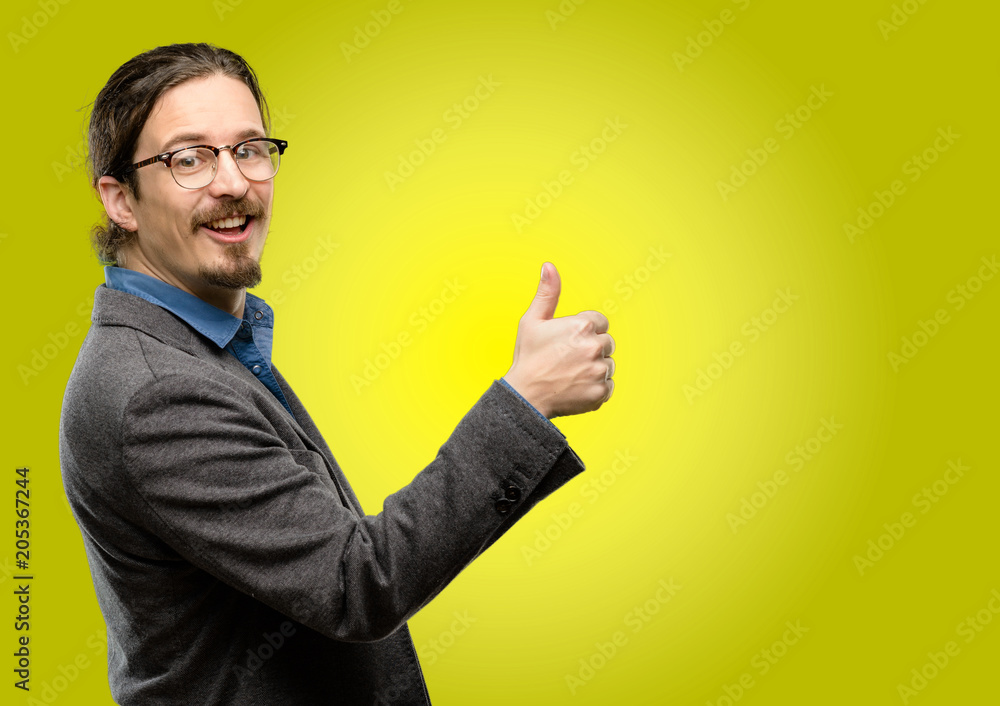 Handsome young man smiling broadly showing thumbs up gesture to camera, expression of like and approval Handsome young man smiling broadly showing thumbs up gesture to camera, expression of like and approval