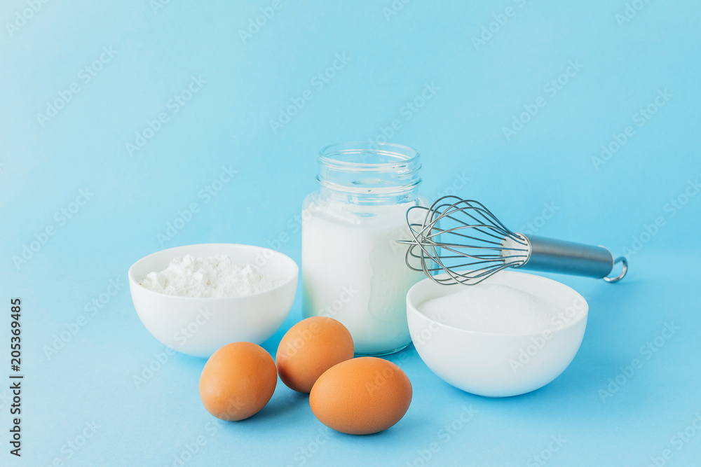 Eggs of chicken, flour in a bowl, sugar, milk in a glass jar whisk ingredient for cooking a bake on a blue background with copy space Eggs of chicken, flour in a bowl, sugar, milk in a glass jar whisk ingredient for cooking a bake on a blue background with copy space