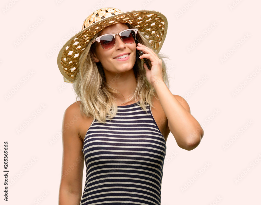 Young woman using sunglasses wearing summer hat happy talking using a smartphone mobile phone Young woman using sunglasses wearing summer hat happy talking using a smartphone mobile phone