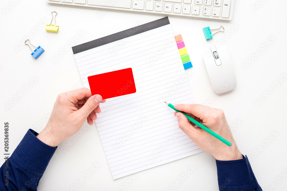 white desktop, male hands, guy writes in a notebook, holding a business card, pensil, notebook, white background with copy space, for advertisement, top view white desktop, male hands, guy writes in a notebook, holding a business card, pensil, notebook, white background with copy space, for advertisement, top view