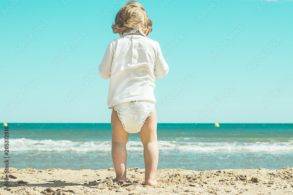 Little girl with diapers on the beach .Children looking at the sea foto