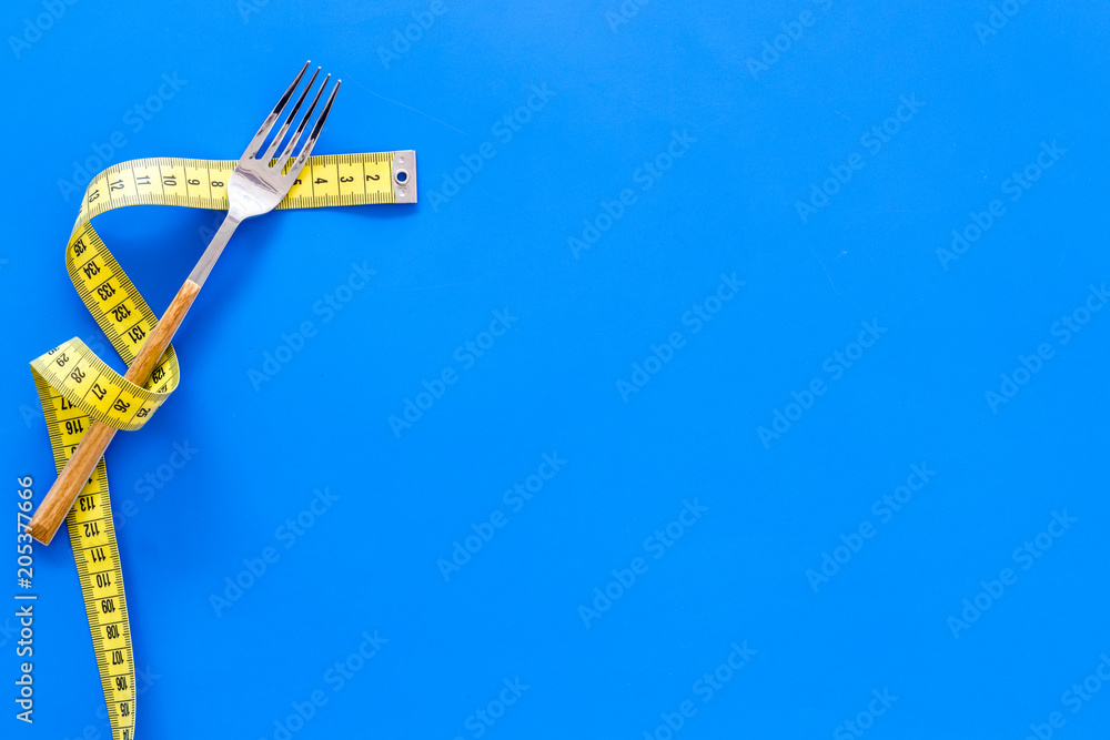 Proper nutrition for slimming. Fork and knife with wound measuring tape on blue background top view copy space