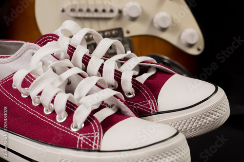 Red sneakers and blurred guitar in background. Close up, selective focus. Rock and Roll fashion concept image