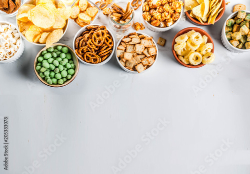 Variation different unhealthy snacks crackers, sweet salted popcorn, tortillas, nuts, straws, bretsels, white marble background copy space