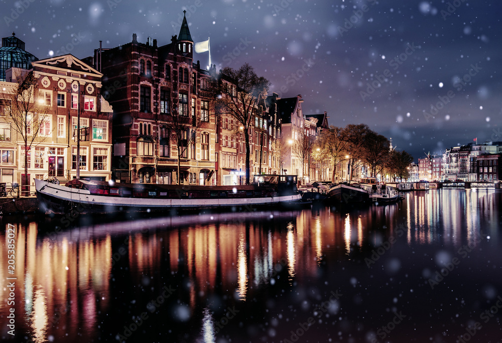 Beautiful night in Amsterdam. Night illumination of buildings and boats near the water in the canal during a snowstorm. Bokeh light effect, soft filter