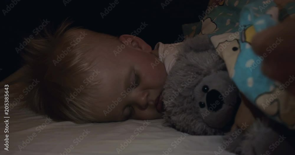 A little boy (son) is sleeping sweetly, blond, mother gently stroking her son, a gray bear toy, in the dark. Concept: children, kids, baby, love, caring family. A little boy (son) is sleeping sweetly, blond, mother gently stroking her son, a gray bear toy, in the dark. Concept: children, kids, baby, love, caring family.