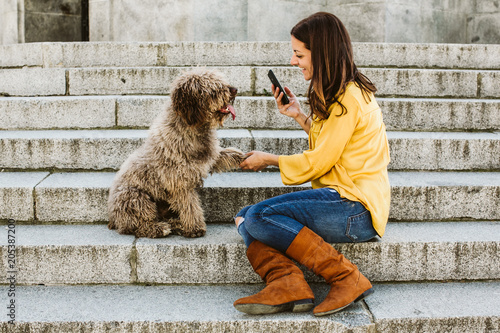 Young beautiful woman taking photograph of her sweet dog playfuly in a lovely park of the center of Madrid. Seated in stone stairs. Lifestyle photo