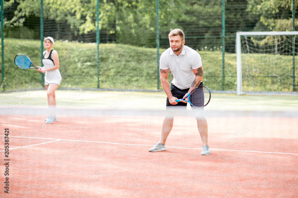 Young couple in white sports wear playing tennis on the tennis court outdoors