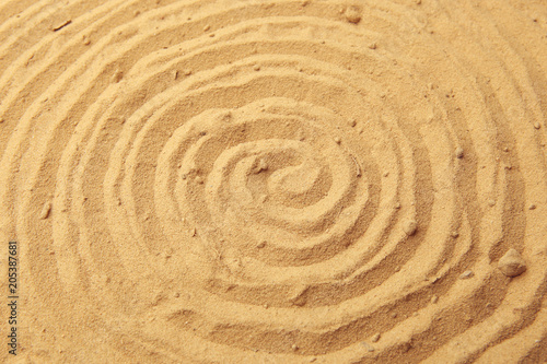 Spiral drawing on beach sand background. Spiral pattern on golden sand. Sand texture.