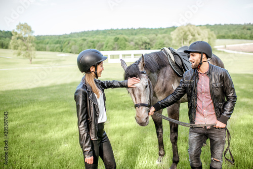 Young couple riders standing near the beautiful horse on the green meadow © rh2010