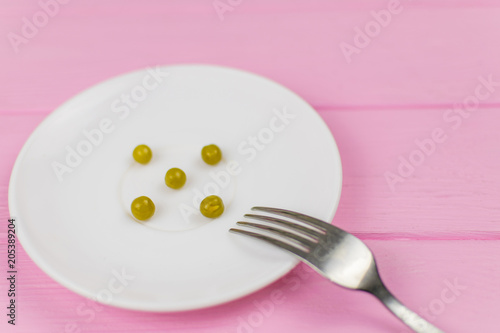 The concept of starvation, bulimia. A few peas on a white plate and a fork.