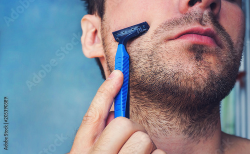 Young man shaving his beard with a razor photo