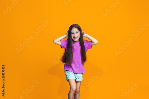 The happy teen girl standing and smiling against orange background. © master1305