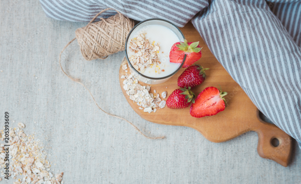 a glass with yogurt oatmeal flakes, pieces of strawberries and a bunch of acacia on a wooden cutting board. a glass of milk with strawberries.