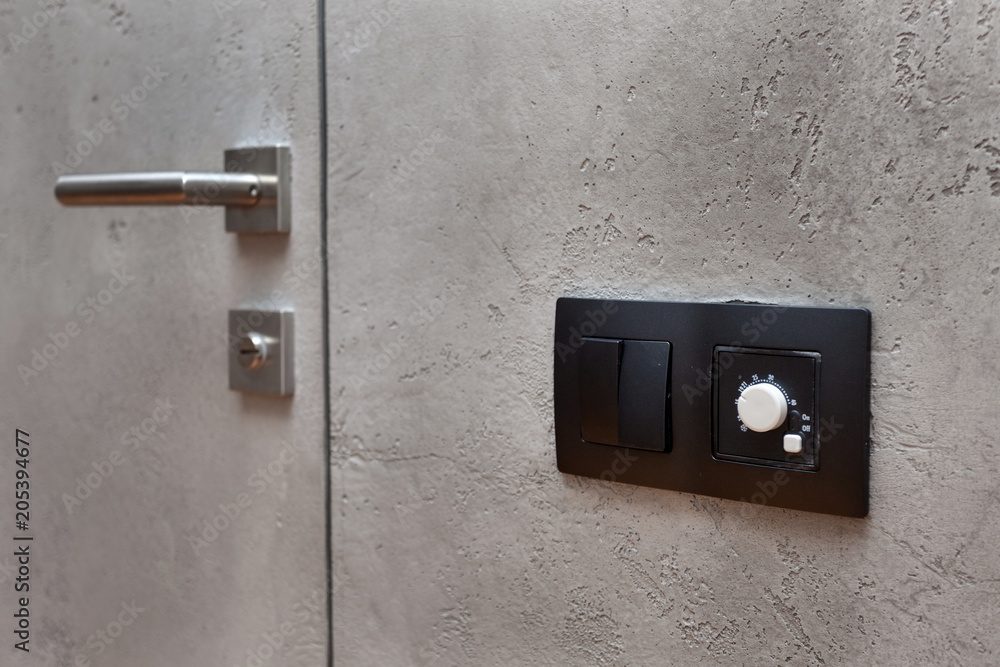 Obraz premium Light switch on the gray textured wall next to the door with metallic handle. Wall temperature regulator located near the door to the room