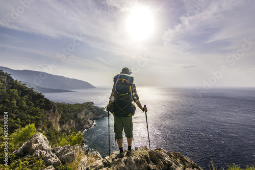 tourist with backpack standing on a cliff in mountains near mediterranean sea