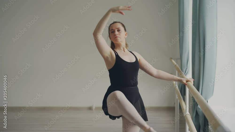 Cheeful adult woman professional ballerina is doing exercises at ballet bar stading on tiptoes, raising leg, doing pirouette. People, art and dancing concept. Cheeful adult woman professional ballerina is doing exercises at ballet bar stading on tiptoes, raising leg, doing pirouette. People, art and dancing concept.