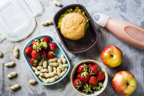 Cooking lunch for the child to school. On the gray kitchen table. Sandwich, strawberries and peanuts in lunchboxes. Top view.