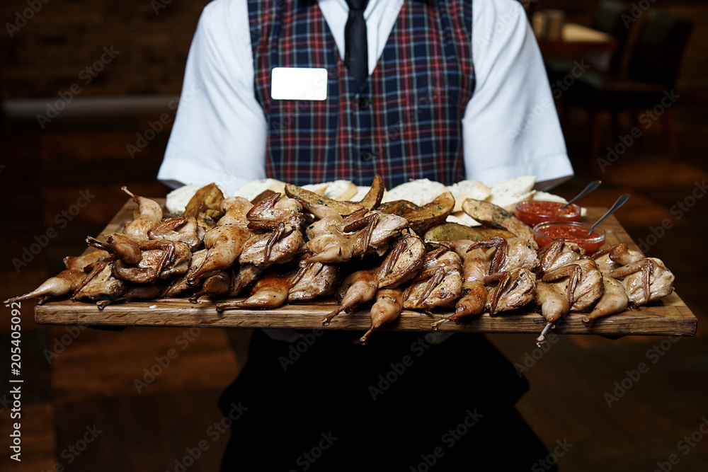 A pile of fried quails on a wooden board in the hands of a waiter.