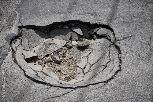 Pit with rubbish and stones on the asphalt road with cracks.