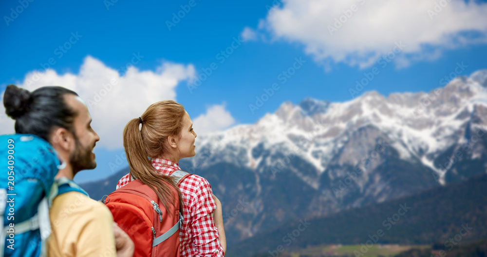 travel, tourism, hike and adventure concept - couple of travelers with backpacks over alps mountains background travel, tourism, hike and adventure concept - couple of travelers with backpacks over alps mountains background
