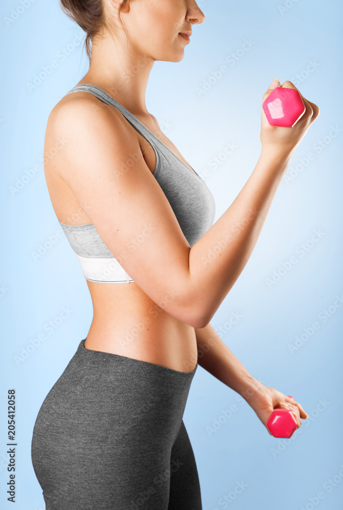 Fitness girl working out with dumbbells. Athletic young woman body isolated on a blue background. Fitness and workout concept Fitness girl working out with dumbbells. Athletic young woman body isolated on a blue background. Fitness and workout concept