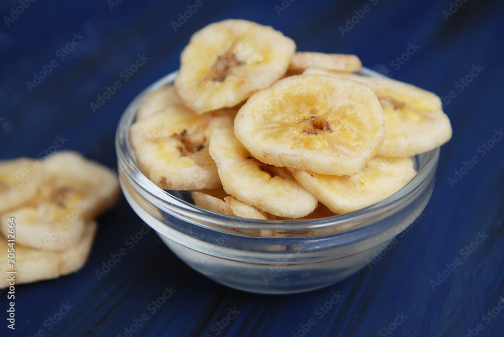 Healthy snack made from Banana Chips. Sliced Banana pieces in Glass bowl on Dark blue Background. Healthy snack made from Banana Chips. Sliced Banana pieces in Glass bowl on Dark blue Background.
