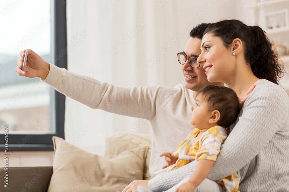 family, technology, parenthood and people concept - happy mother and father with baby daughter taking selfie by smartphone at home