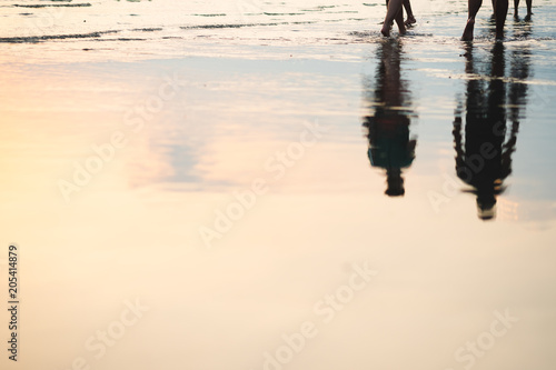 Silhouette of couple walking on beach with drop shadow reflected on sea water surface in sunset.