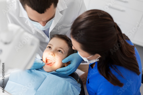 medicine, dentistry and healthcare concept - dentist with mouth mirror checking for kid patient teeth at dental clinic