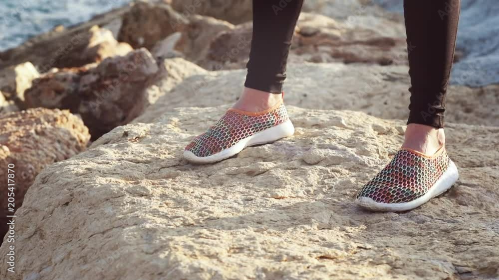 Close-up of slender sports girl doing sit-ups squats by the sea. Female legs in sneakers. Close-up of slender sports girl doing sit-ups squats by the sea. Female legs in sneakers.