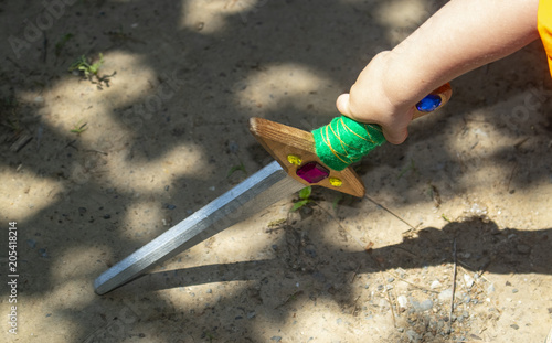 Little boy's arm with colorful toy wooden sword touching ground with dramatic shadows