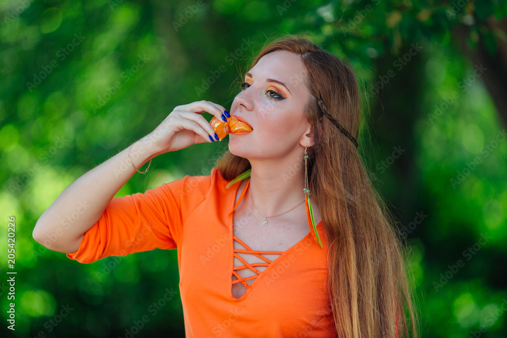 Portrait of pretty red hair woman with juicy delicious orange at summer green park.