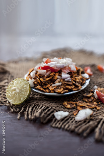 Popular Indian & Asian snack or junk food chana chur garam in a clay bowl on wooden surface with onions,lemon and tomatoes. photo