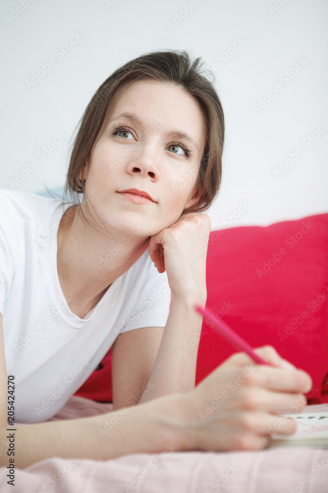 Young woman writing something in the notebook on the bed. Peaceful atmosphere. Young woman writing something in the notebook on the bed. Peaceful atmosphere.