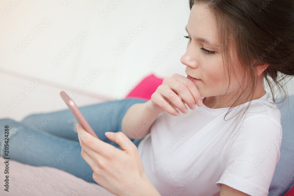 Excited winner checking online the phone for a prize lying on the bed at home with a window in the background Excited winner checking online the phone for a prize lying on the bed at home with a window in the background