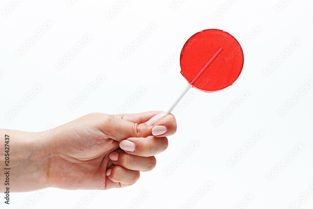 Red round lollipop on a stick in a hand on a white background. Red round lollipop on a stick in a hand on a white background.