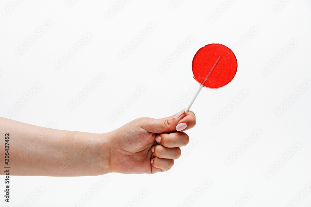 Red round lollipop on a stick in a hand on a white background. Red round lollipop on a stick in a hand on a white background.