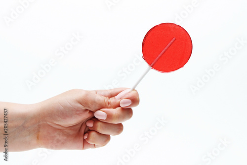 Red round lollipop on a stick in a hand on a white background.