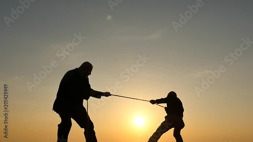 competition concept - tug of war - 2 persons pulls rope silhouettes photo