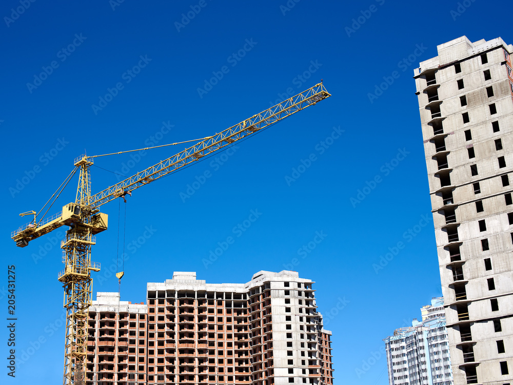 An urban building under construction with cranes against blue sky. An urban building under construction with cranes against blue sky.