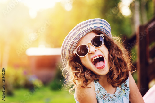 summer portrait of happy kid girl on vacation in sunglasses and hat, laugh and showing tongue.