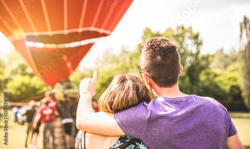 Happy couple in love on honeymoon excursion waiting for hot air balloon ride - Summer travel concept with young people travelers having fun at trip vacation - Bright warm filter with backlight photo