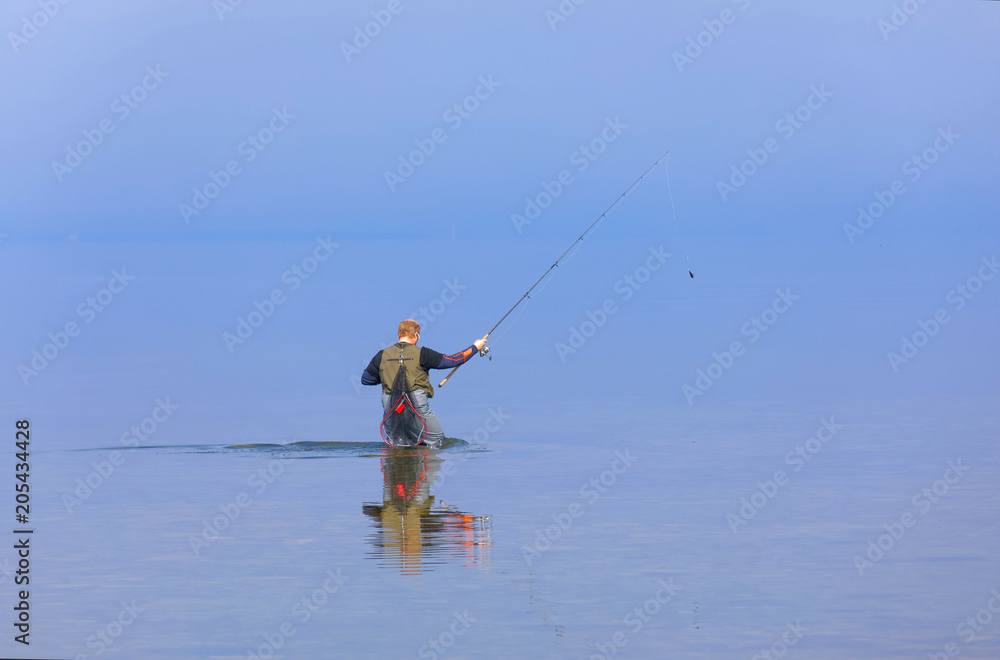 Angler walking in the blue calm sea trying to catch trout at Aleklinta on the island Oland, Sweden Angler walking in the blue calm sea trying to catch trout at Aleklinta on the island Oland, Sweden
