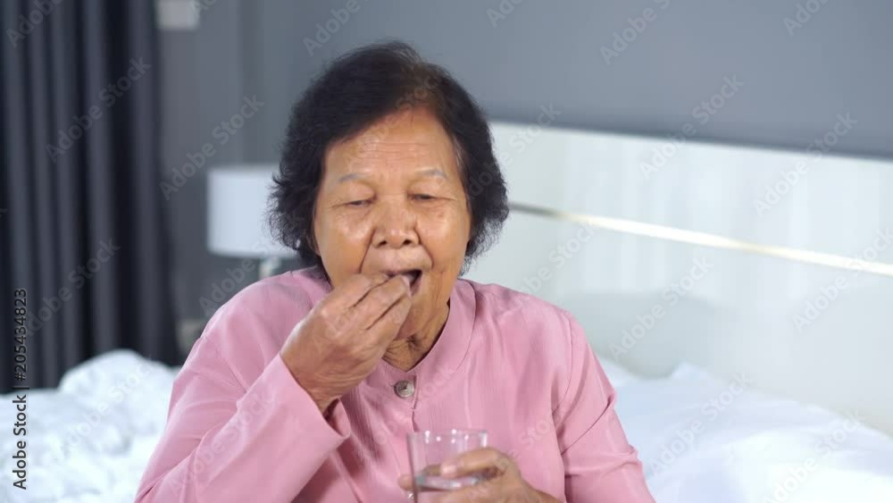 senior woman taking pill with glass of water in bed senior woman taking pill with glass of water in bed