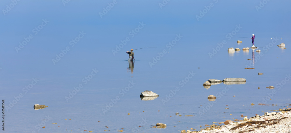 Obraz premium Two angler in the blue calm sea trying to catch trout at Aleklinta on the island Oland, Sweden