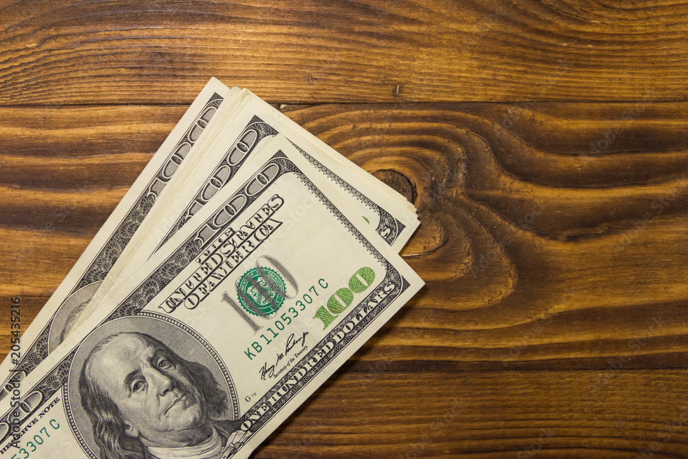 One hundred dollars bills on wooden desk One hundred dollars bills on wooden desk
